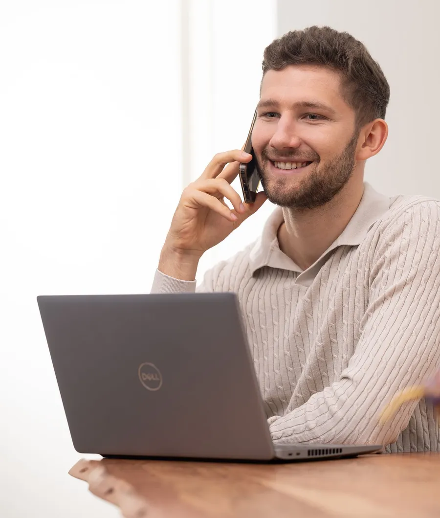 Daniel Wegener lächelnd am Telefon, vor ihm der Laptop